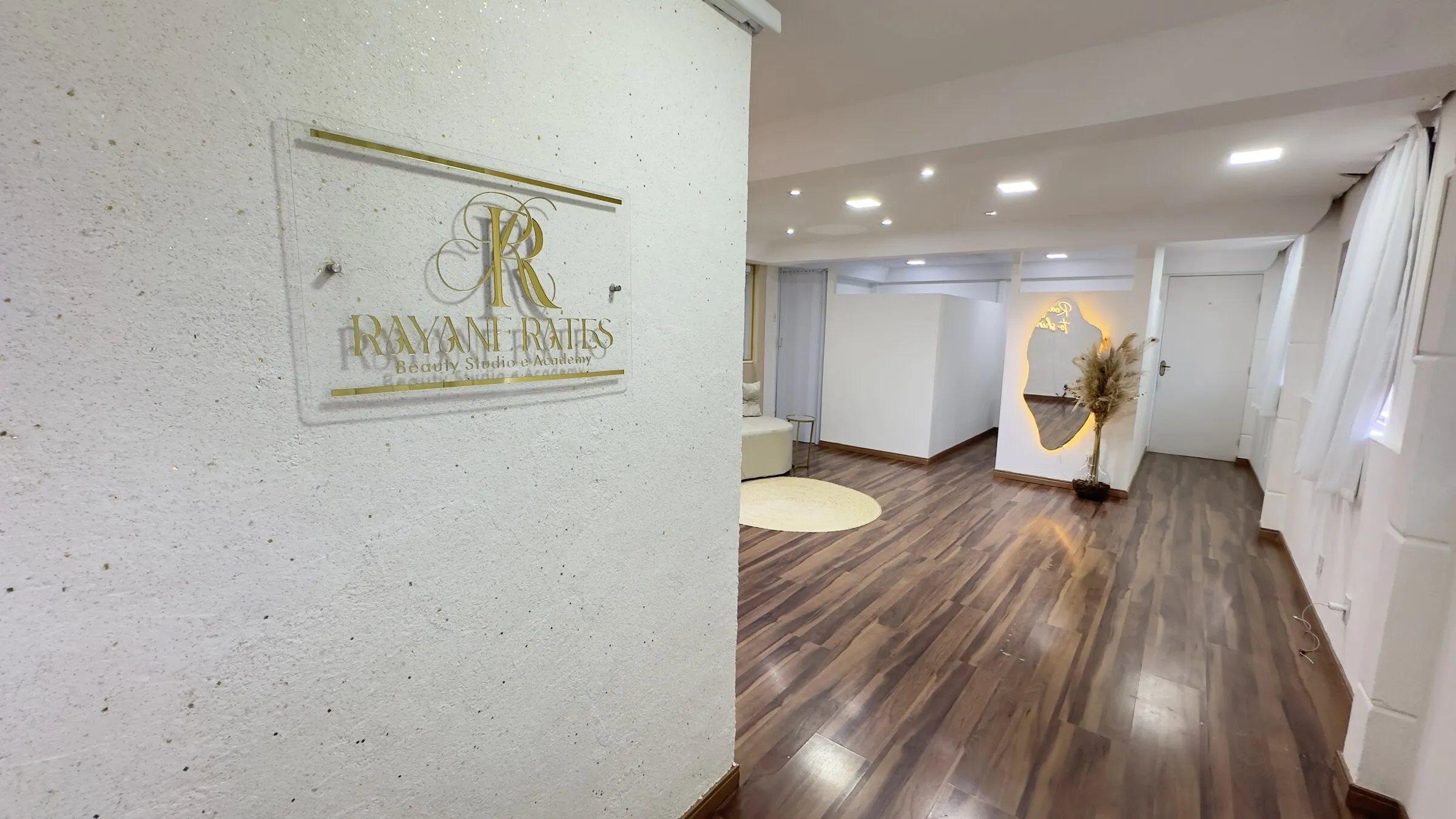 Placa dourada com o logo Rayane Rates Beauty Studio e Academy na parede da entrada